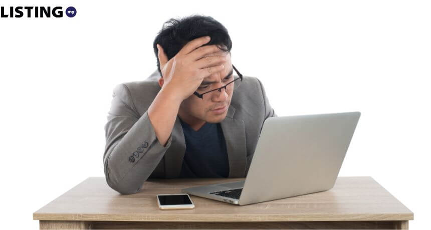 A stressed office worker holding his head in frustration while looking at a laptop screen, depicting computer problems or work pressure.
